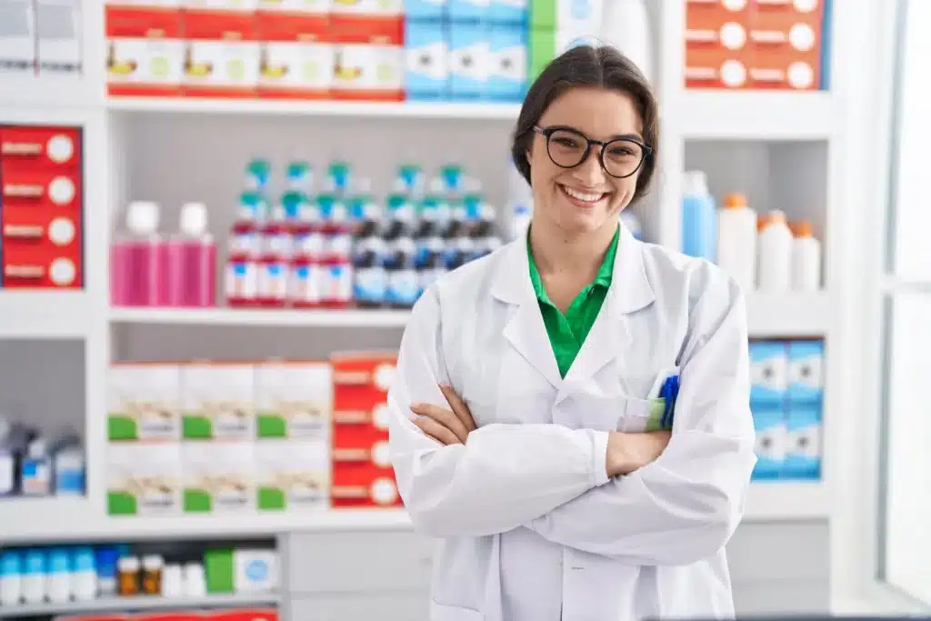 Farmaceutka w aptece uśmiechająca się do kamery.